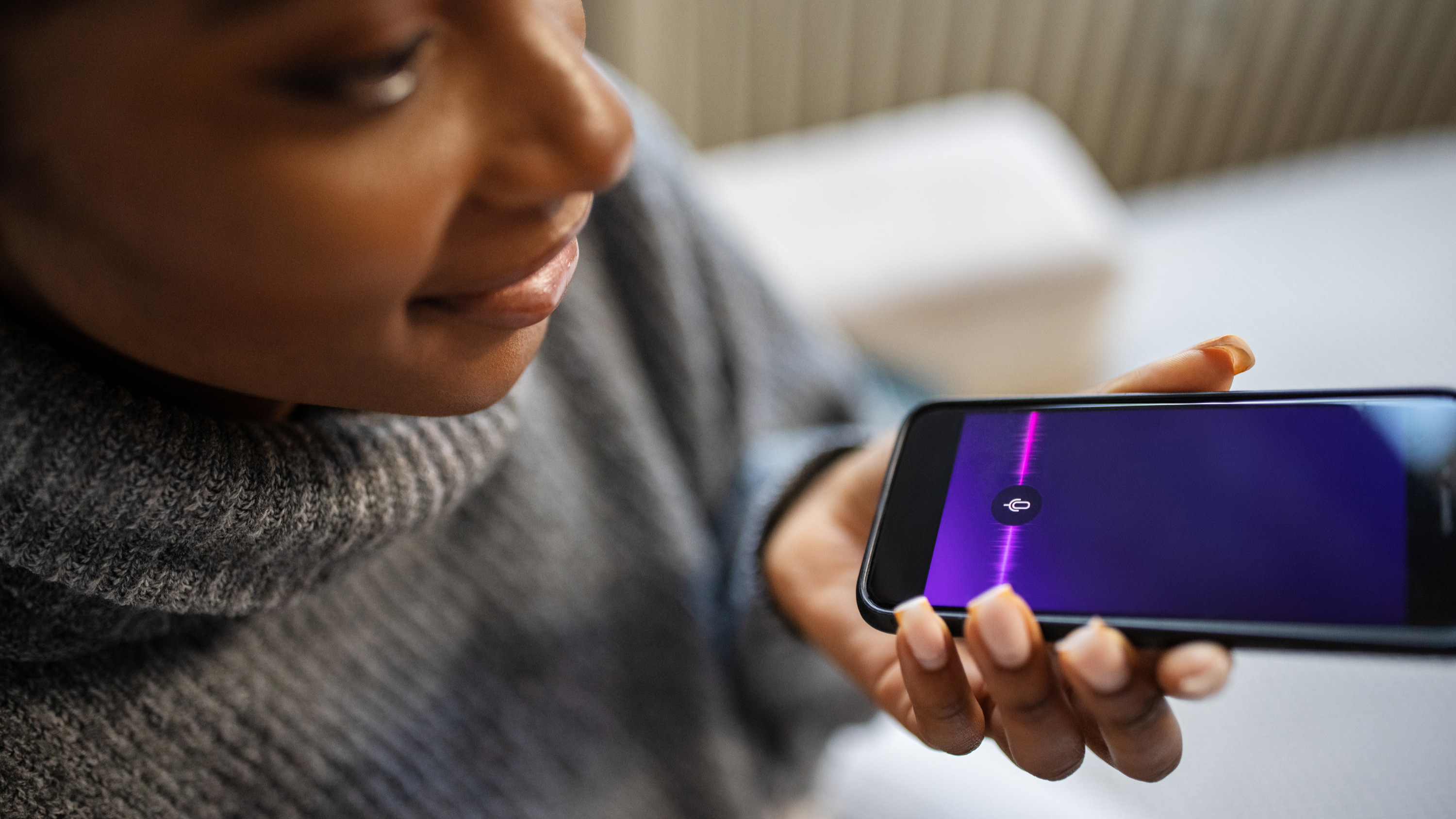 אישה מחזיקה סמארטפון עם גל סאונד על המסך - אפליקציות AI לבריאות נפשית